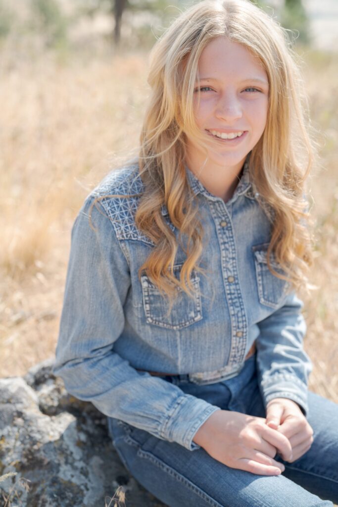 Young blonde girl in a denim jacket and blue jeans smiles at Robin Jolin's camera.