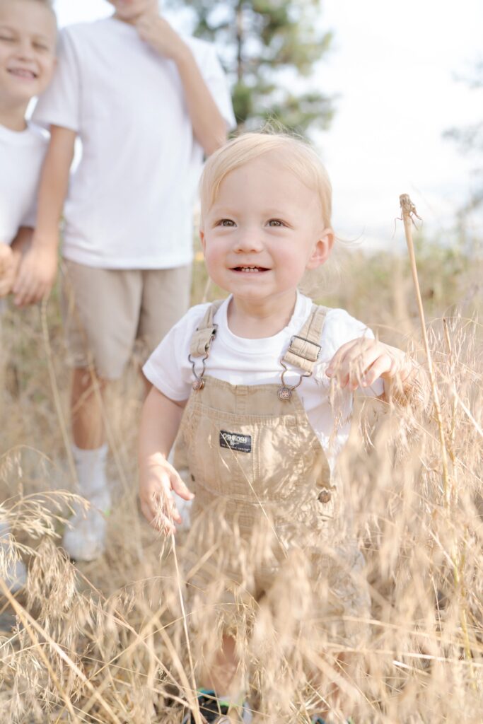 Young newborn boy dressed gentlemanly touches the dried tall grass in La Grande, Oregon.