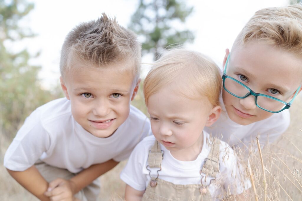 Two young boys pose behind their even younger sibling who finds the whole thing confusing.