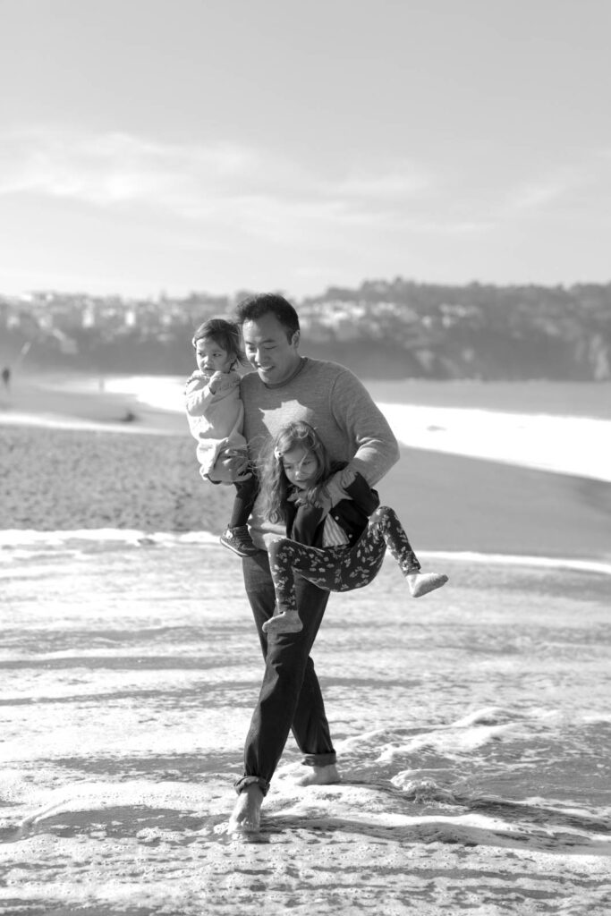 A father lifts her daughters at the shore in Baker Beach, shot by San Francisco family portrait photographer Robin Jolin.
