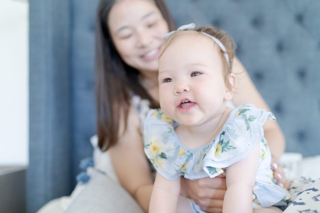 Cute baby with tiny teeth wears a cute flowery-dress and tries to talk while her mom holds her.