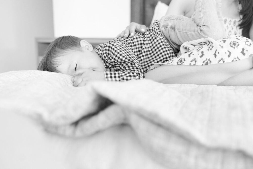 Baby boy hugs the bedsheet besides his mother.