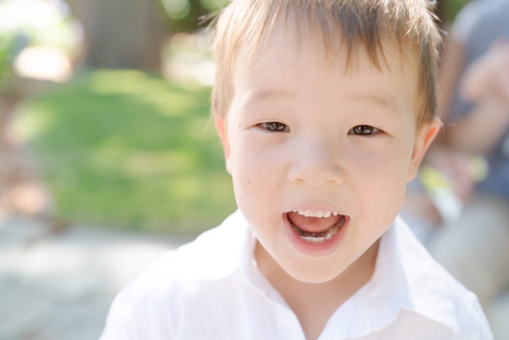 Little boy in a white shirt opens his mouth and shows his teeth.