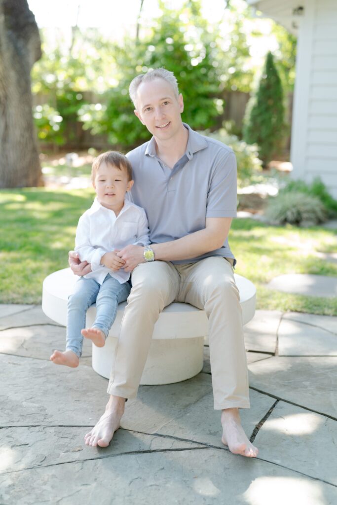 Cute boy in blue jeans and a white shirt sits obediently besides his father.