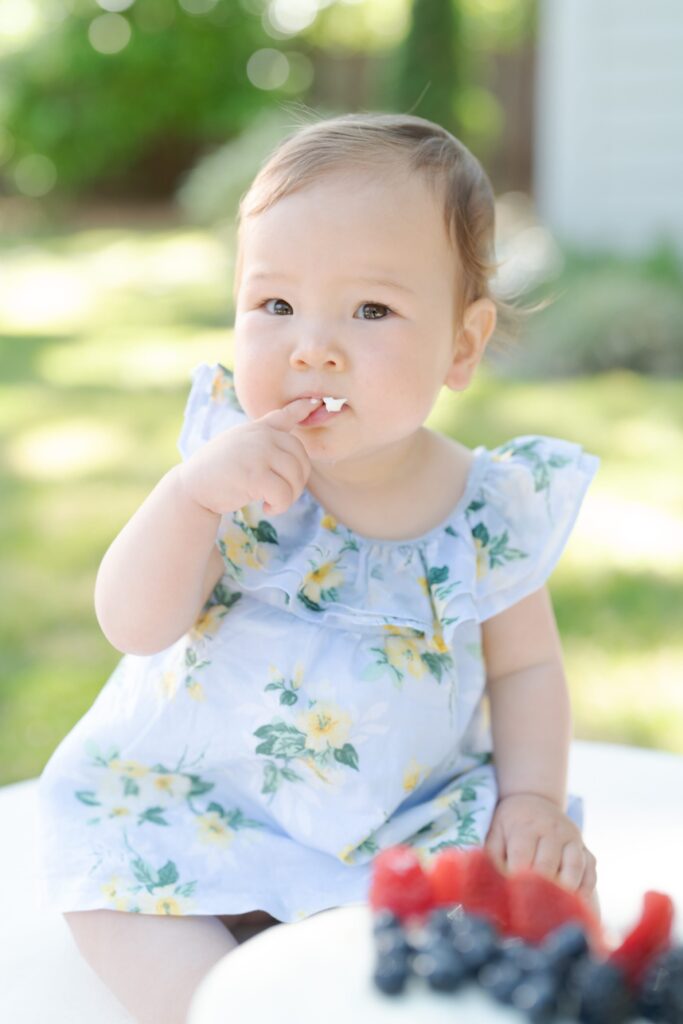 Baby daughter shoves cake in her mouth with her little baby fingers.