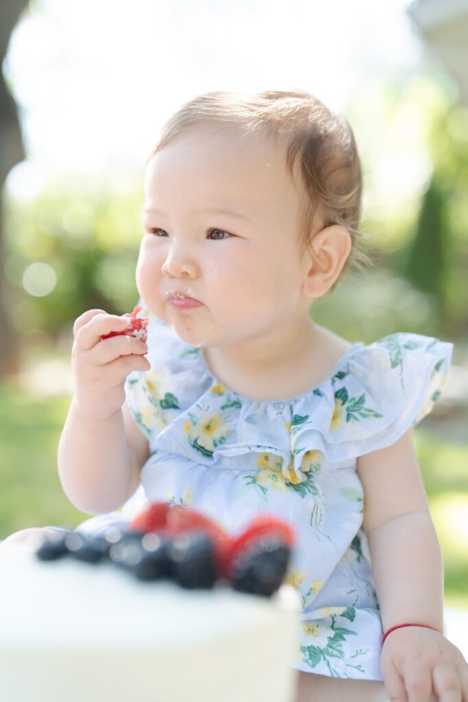 Baby daughter squints while eating a strawberry.