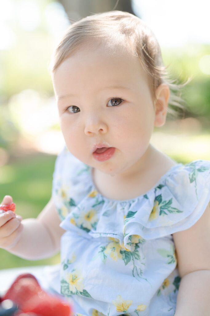 Beautiful newborn baby girl holds a strawberry and looks at Robin Jolin's camera.