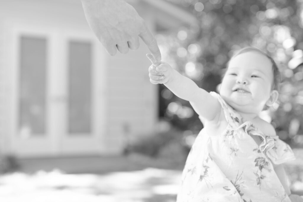 Baby girl lifts her index finger and tries to touch her dad's index finger.