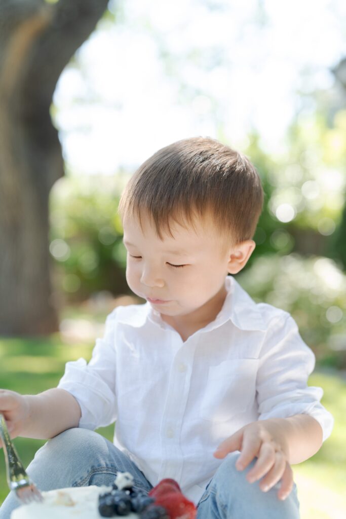 Baby boy in a white shirt and blue jeans moments before devouring a white cake.