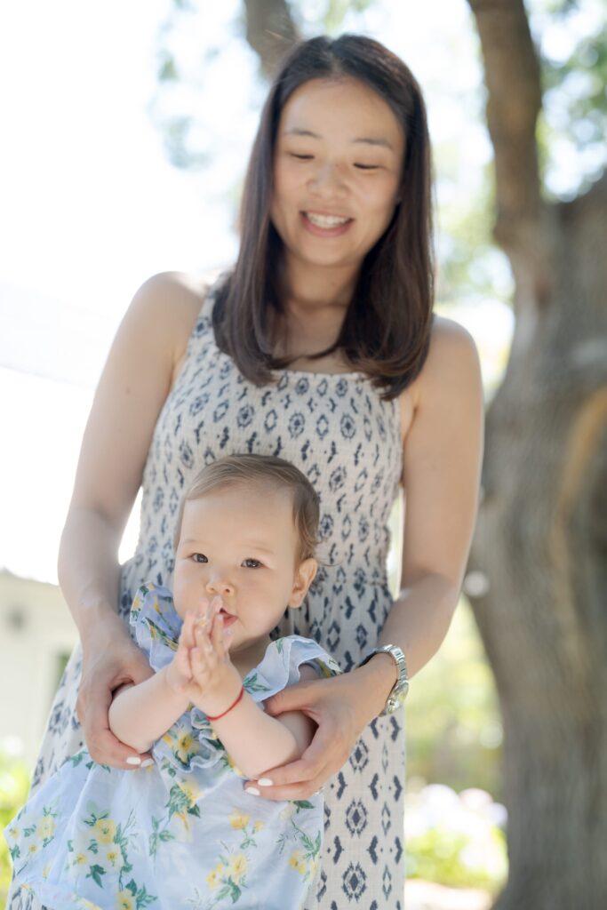 Happy mother holds her daughter and watches her join hands, as if greeting 'Namaste'