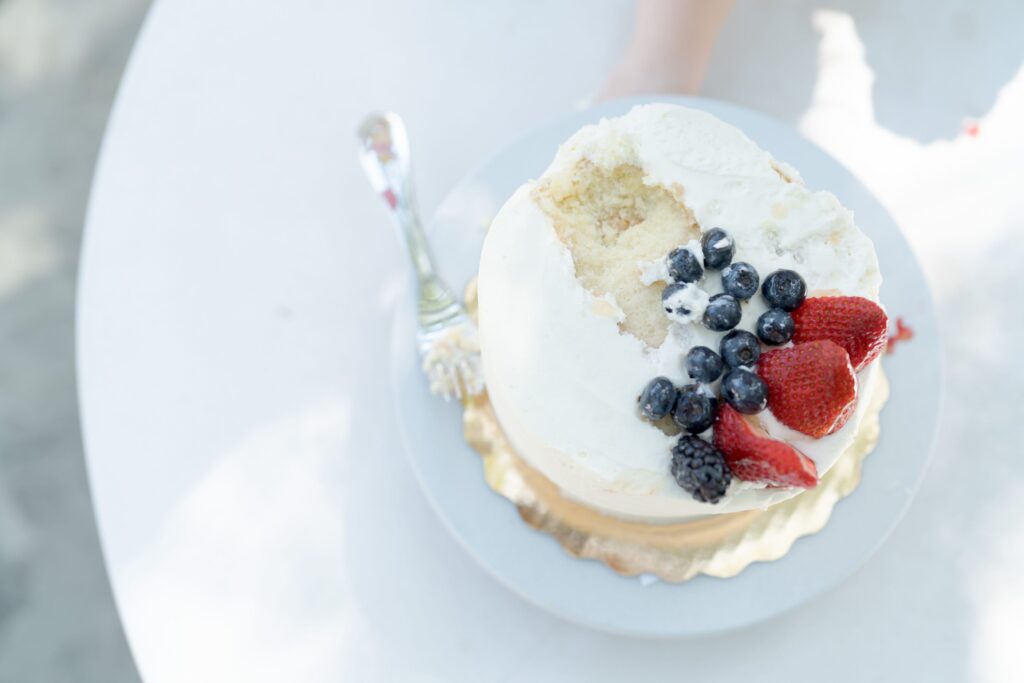 The white cake with red and black berries after the children devoured its middle part.