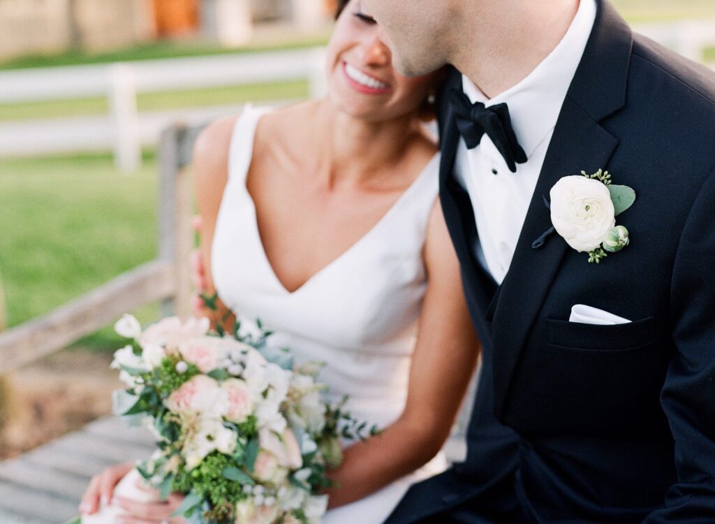 Newly married bride holds a rose bouquet as her new husband embraces her.