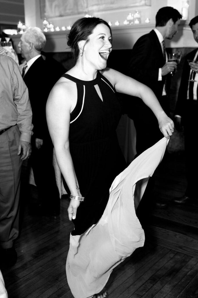 Lady in black dancing at a wedding party while men hold their drinks in the background.