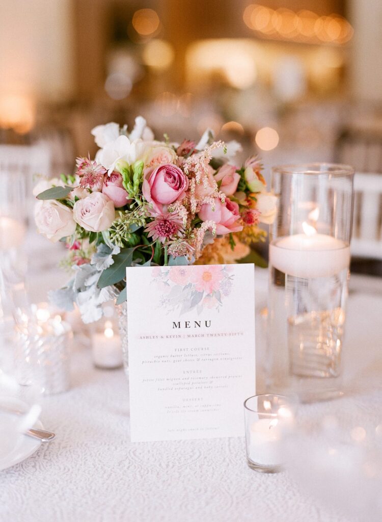 Beautifully decorated table at a wedding with a rose vase and scented candles.