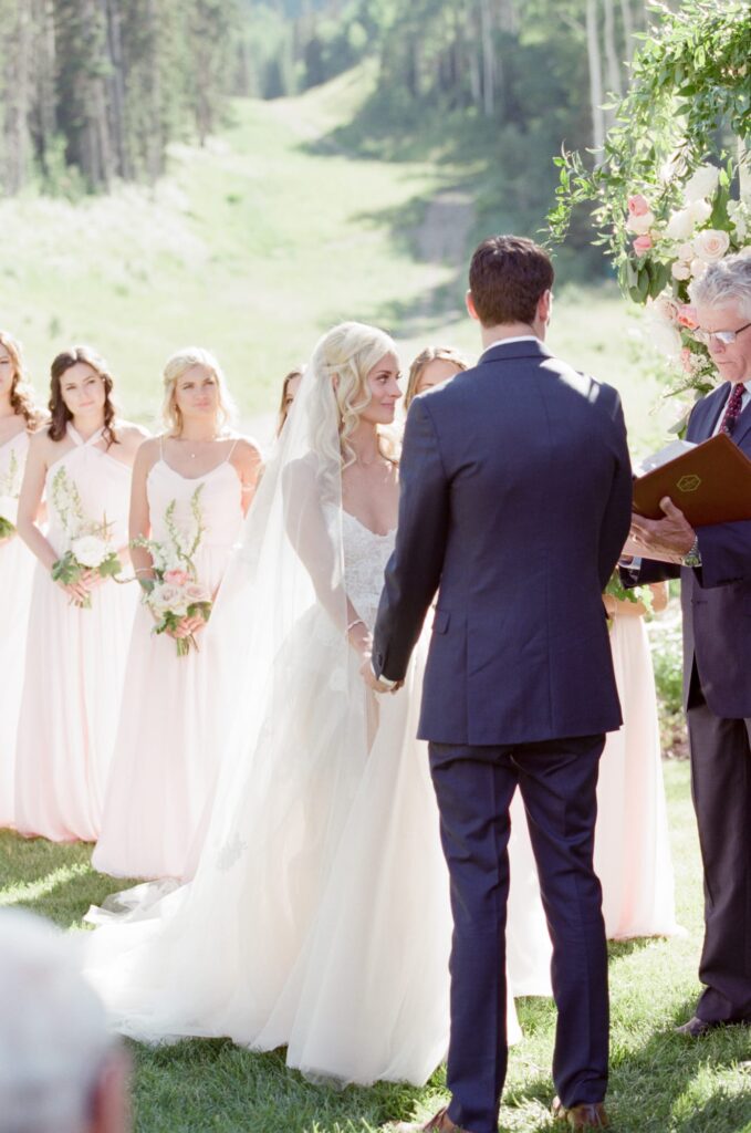 Wedding couple exchange vows in pronouncement ceremony with bridesmaid watching in the background.
