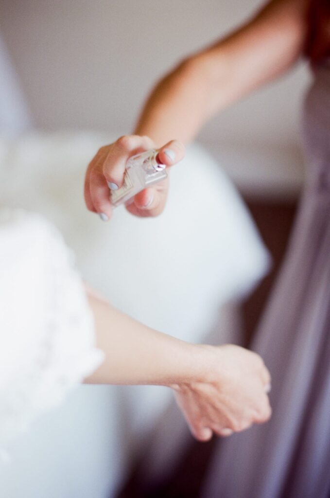 Bridesmaid puts cologne on the bride's wrist.