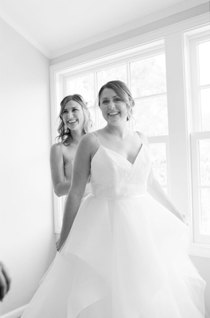 Bride proudly smiles with her bridesmaid while wearing her wedding gown.