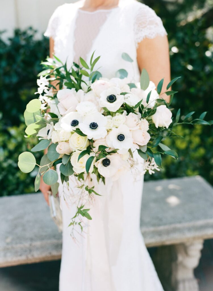 White flower bouquet held by a bride in white wedding attire.