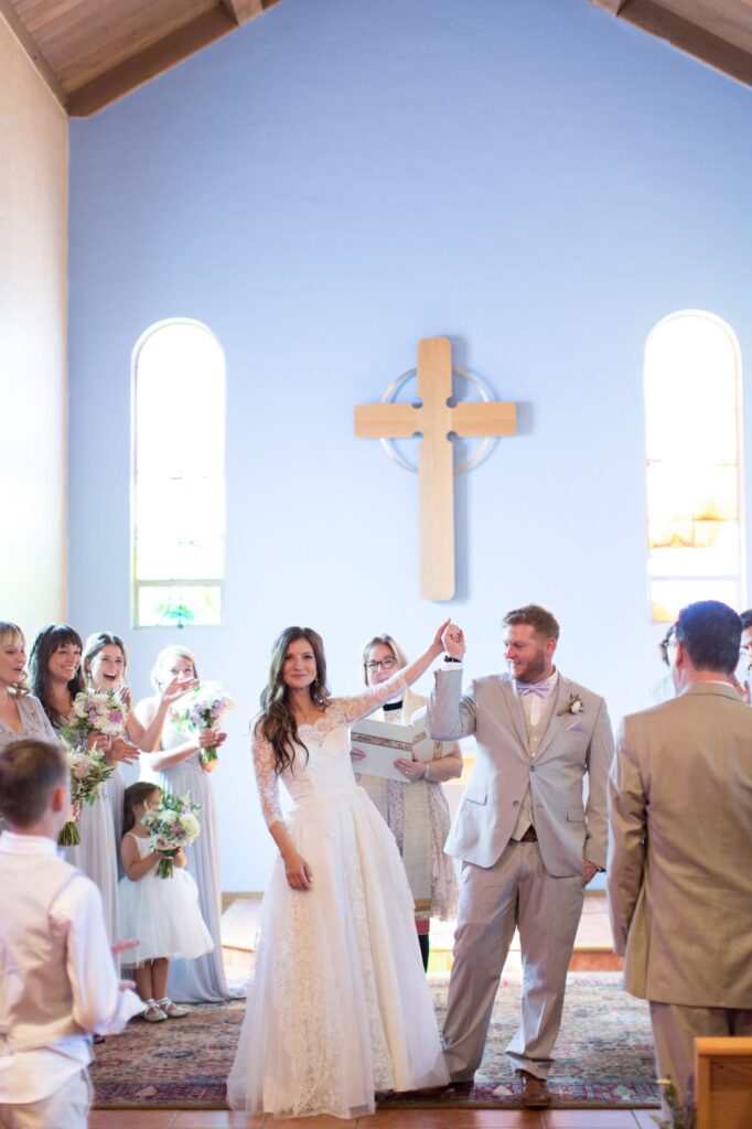 Groom lifts his wife's hands during the wedding ceremony in a church.