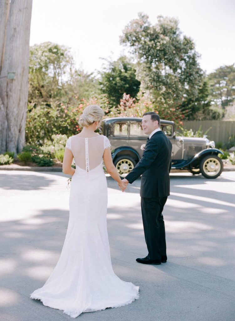 Groom leads his bride to a vintage car.