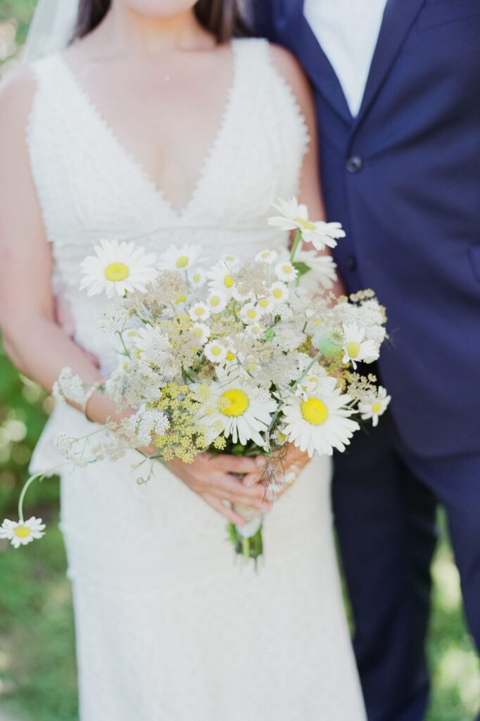 Bride holds a bouquet of daisies with her husband.