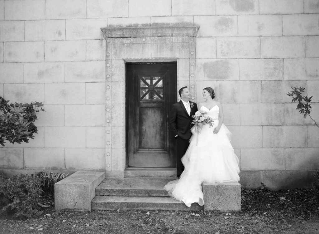 Elegant bride and groom stand in front of a tall estate.