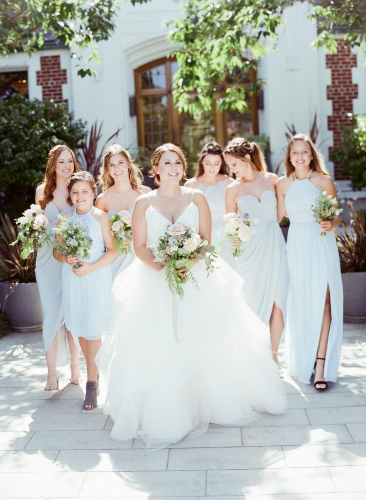 Bride with her bridesmaids stand in elegant wedding gowns.