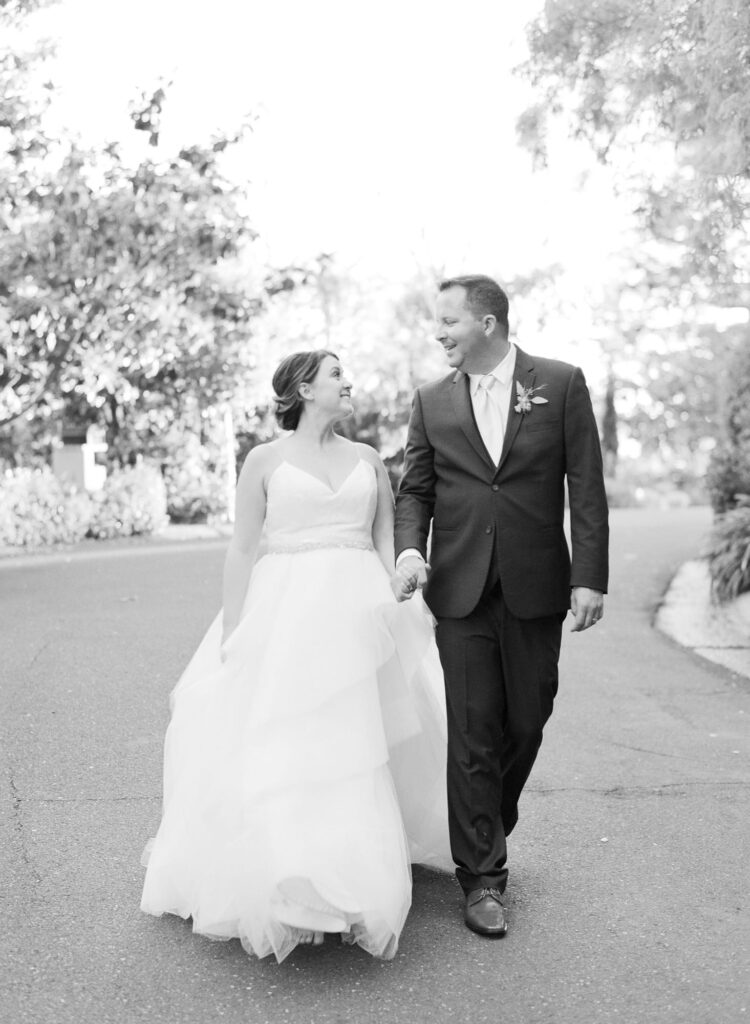 Newly married bride and groom walk down a paved road.