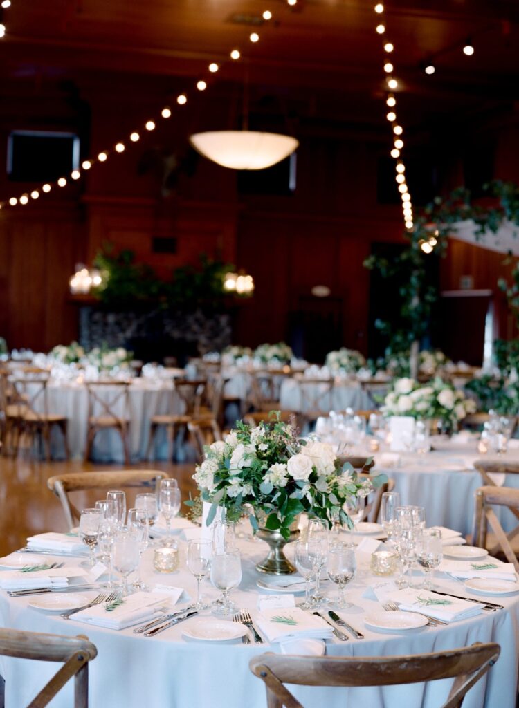 Wedding reception dining tables with cutlery and a white flower vase.