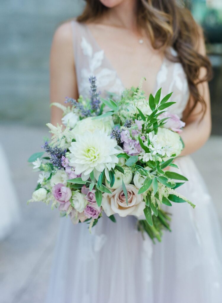 Bride in wedding attire holds a pretty flower bouquet.