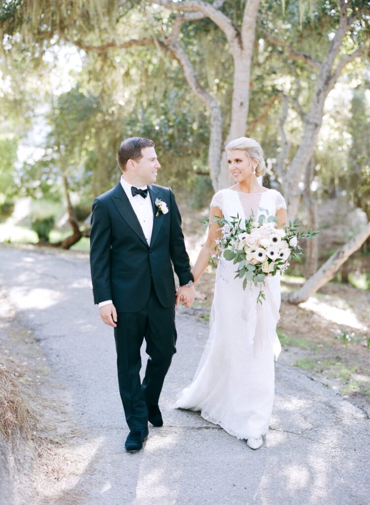 Newly-wed couple hold hands and walk down the narrow path.