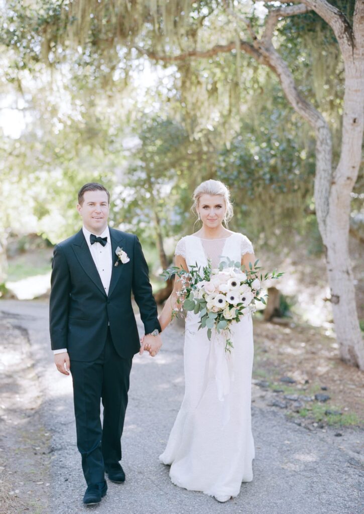 Newly-married couple hold hands and walk down the narrow path.