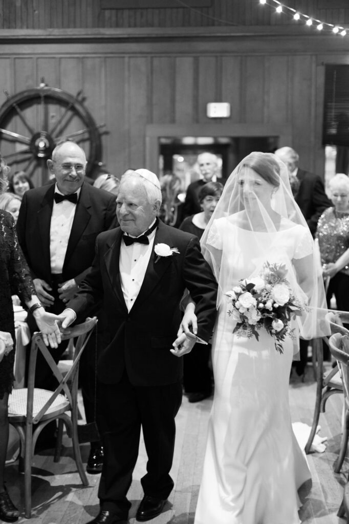 Father presents his daughter bride in wedding attire wearing a veil.