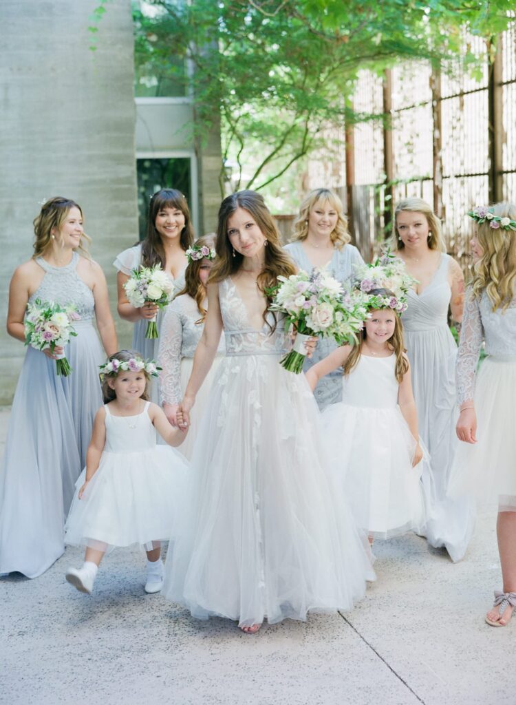 Bridesmaids and cute little girls stand behind the bride who holds her bouquet.