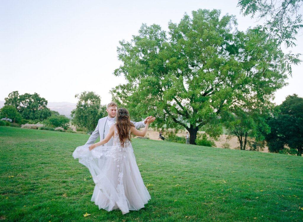 Aesthetic image of bride and groom dancing in wedding attires at a garden.