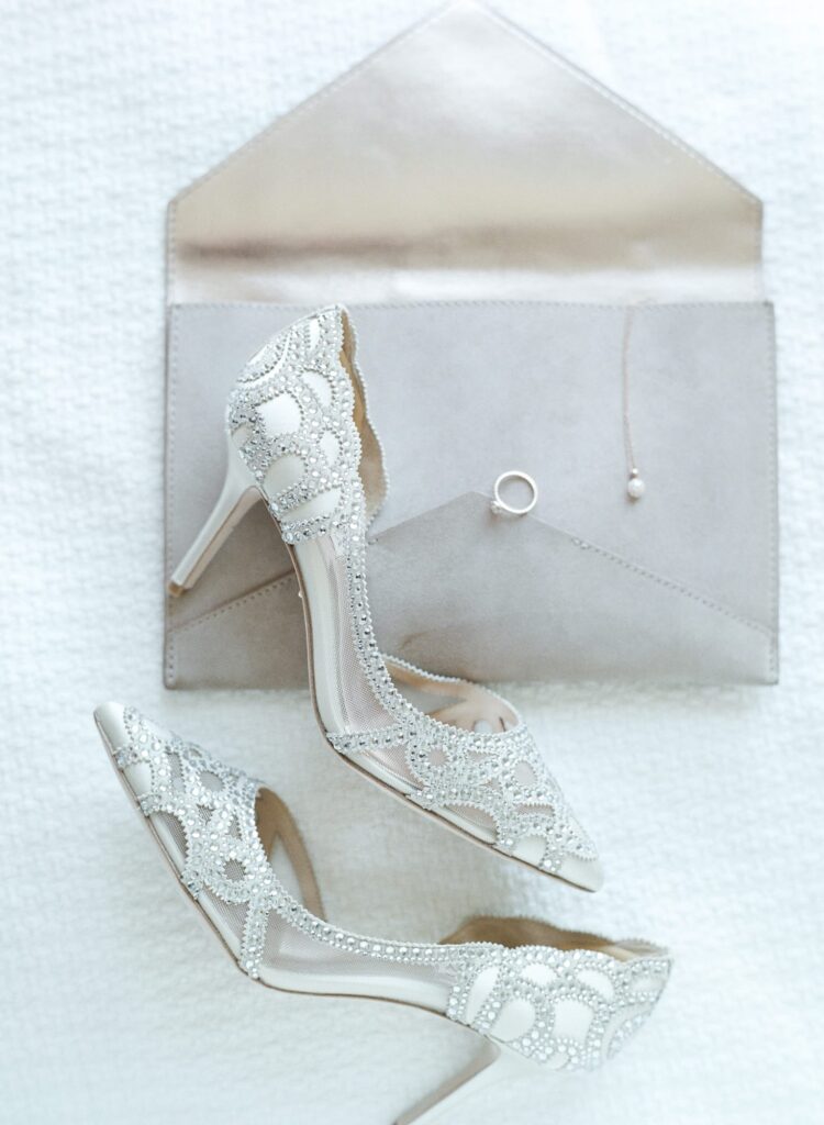 Pretty white wedding sandals on a white tabletop and an envelope with ring.