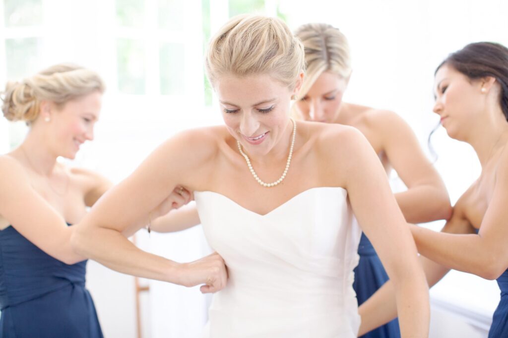 Bridesmaids help bride-to-be with her wedding gown.