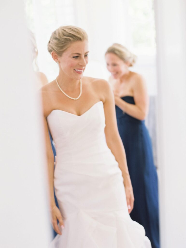 Bride smiles in front of her bridesmaid.