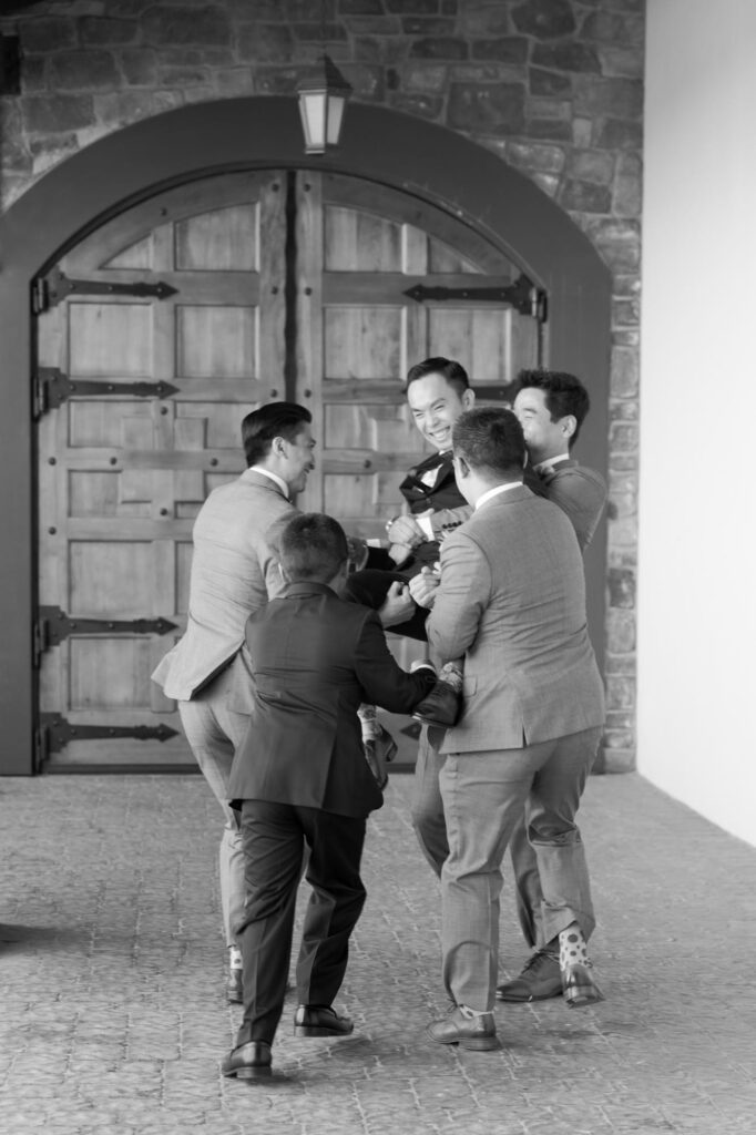 Groomsmen joyfully lift their groom.