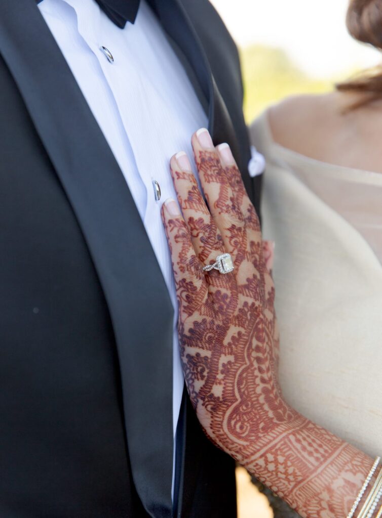 Bride places her hand on her husband's chest. The hand has mehendi and a wedding ring.