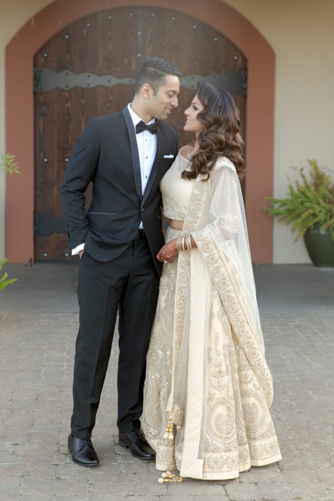 Bride in off-white lehenga and groom in a tuxedo embrace each other before the afterparty.