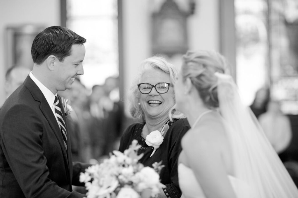 Bridegroom in a dark suit with a striped tie, bride's mother with short blonde hair and glasses, and the bride in a wedding dress with a veil