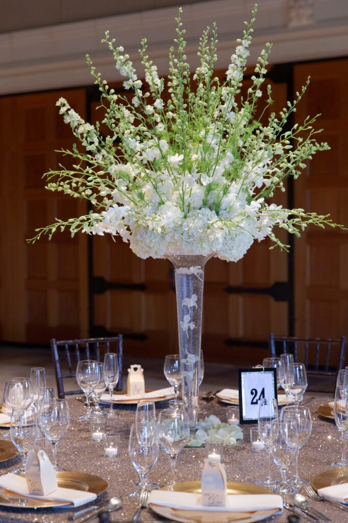 Table and cutlery arrangement with a tall vase of white flowers in the middle.