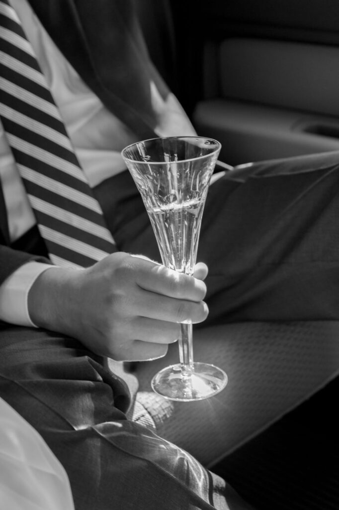 Elegantly dressed man in suit and tie holds a classy glass of champagne.