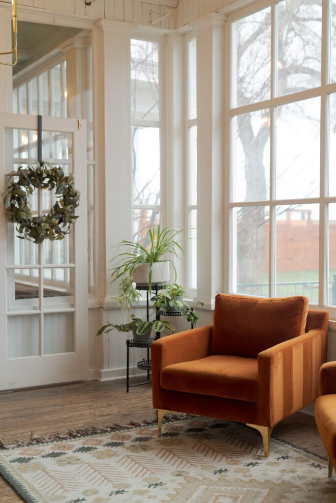 An interior view of a sunlit room with large windows. The room features an orange armchair with a modern design.