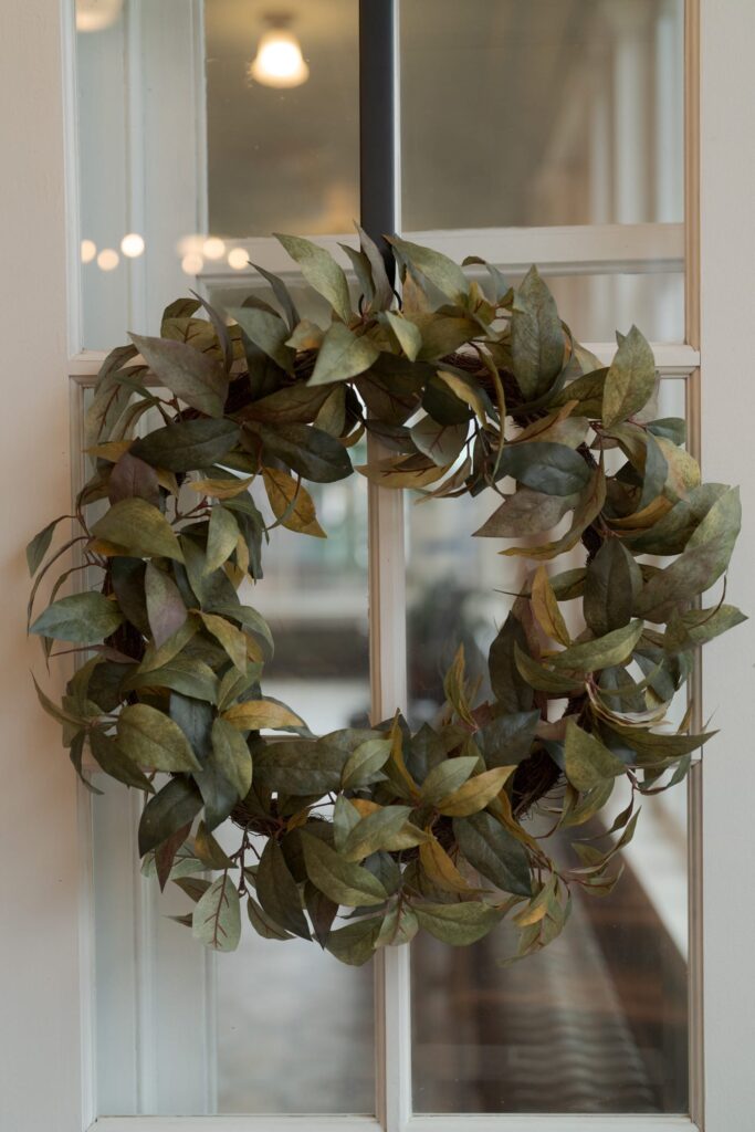 A close-up view of a green wreath made of leaves hanging on a glass-paneled door.