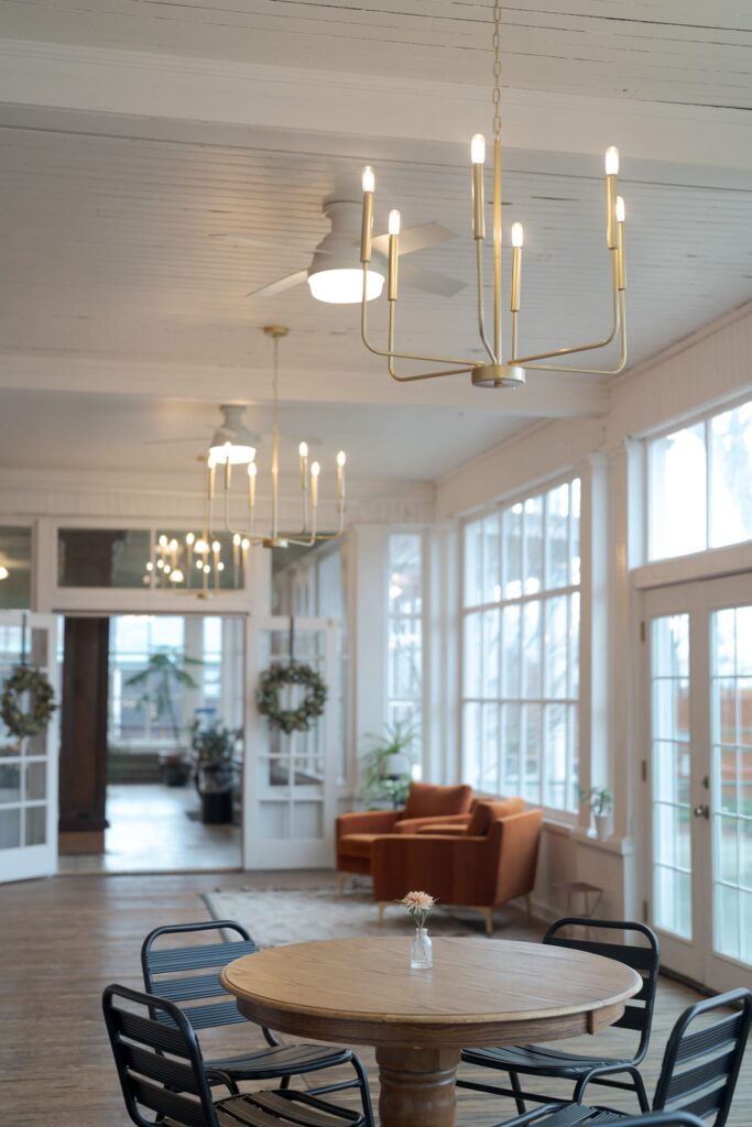 Modern chandeliers, an orange armchair, a round wooden table with a small flower vase, and black metal chairs.