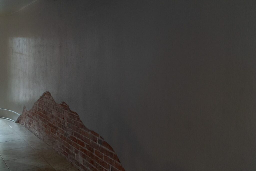 Hallway with a partially exposed brick wall, contrasting against a mostly smooth, dark-painted surface.