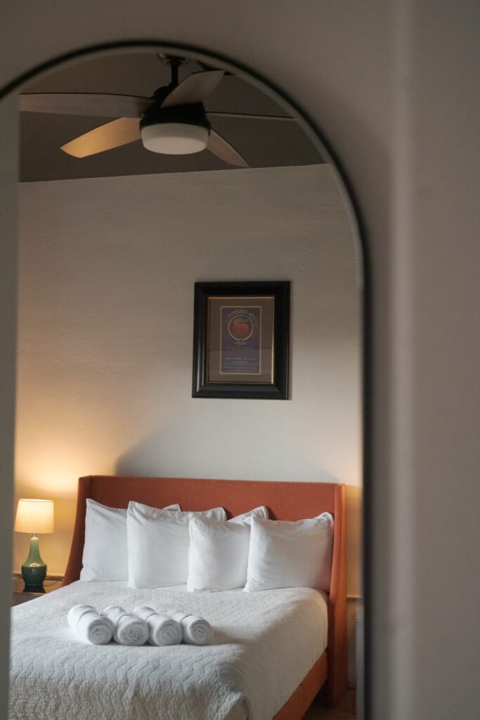 A bedroom with an orange bed frame with white bedding and four neatly arranged white pillows.