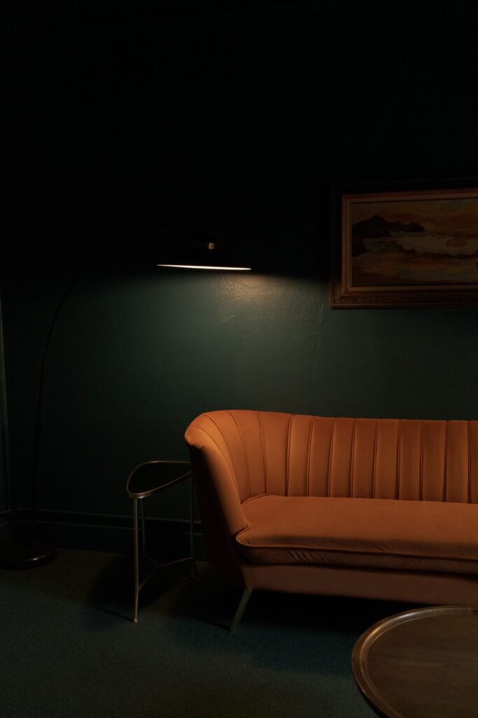 Retro-style orange sofa dimly lit by a modern wall-mounted lamp